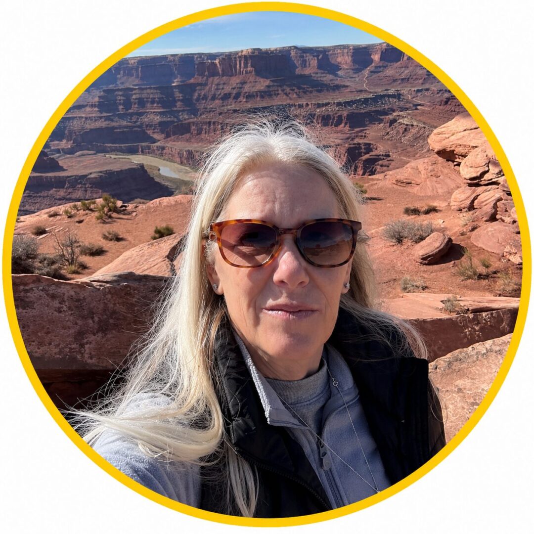 Woman with long gray hair and sunglasses at a scenic desert canyon.
