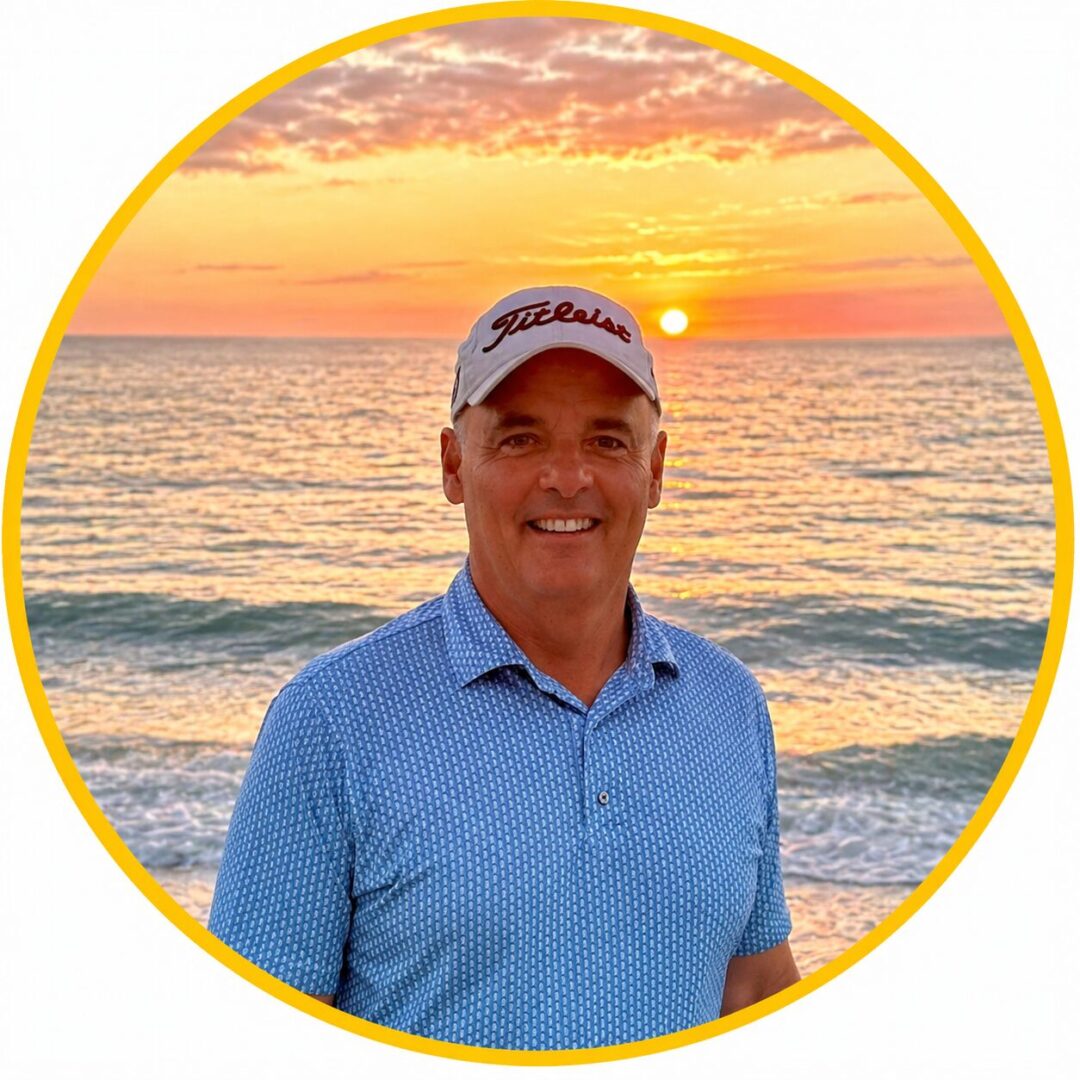 Man in a blue shirt and cap smiling by the ocean at sunset.